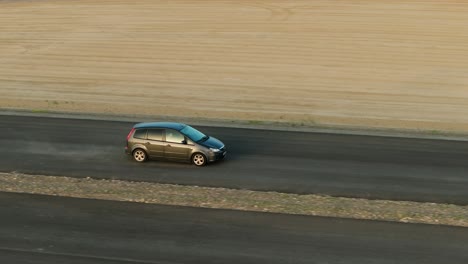 grey car driving on an unfinished tarmac road, accelerating rising trail of dust behind, aerial close up tracking shot