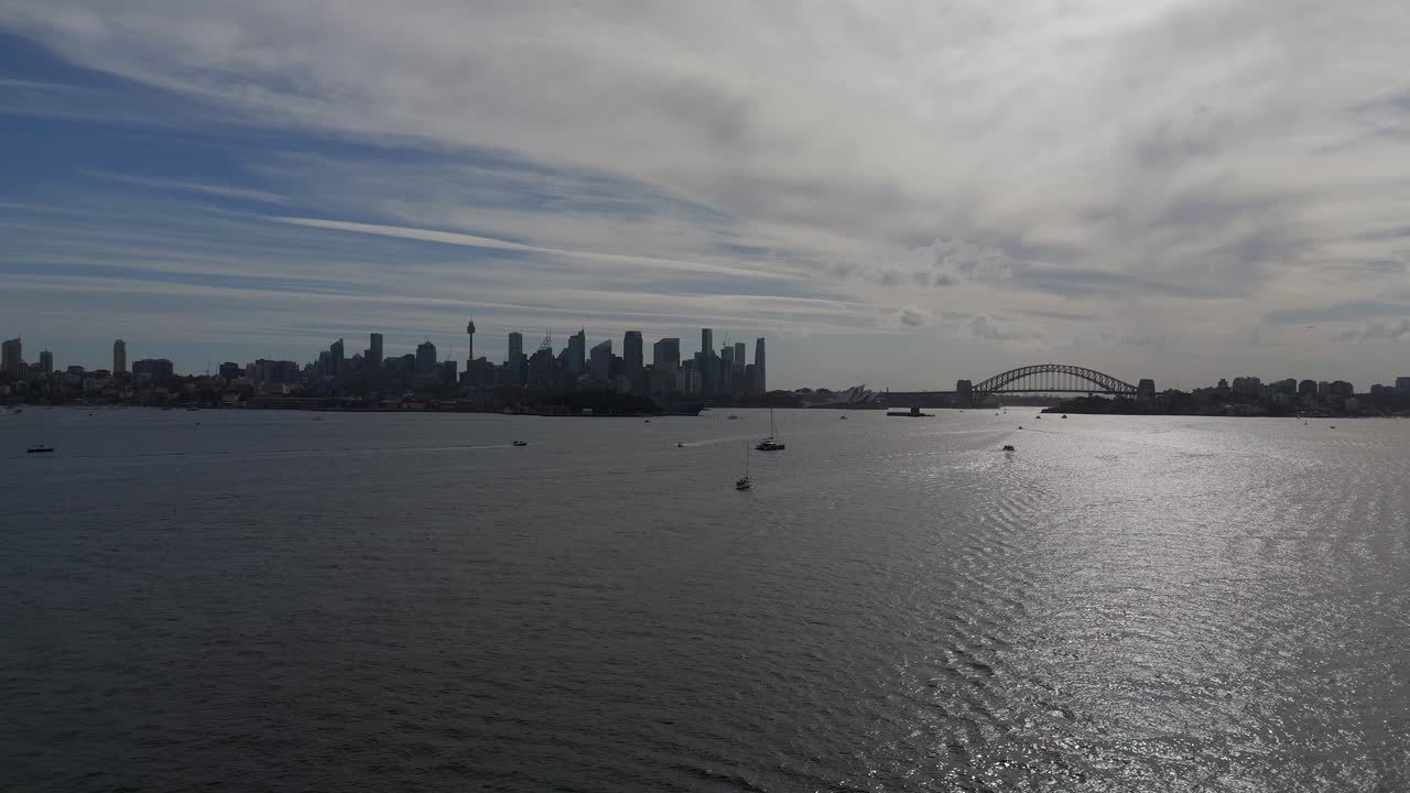 Skyline of Sydney with skyscrapers and boats on water. Aerial rising wide shot. Sunny day with silhouette of high-rise buildings in Background. Australian Metropolis with Sydney Harbour Bridge.