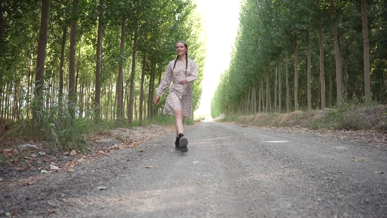 Una donna cammina su una strada polverosa splendidamente circondata da alberi verdi e rigogliosi.