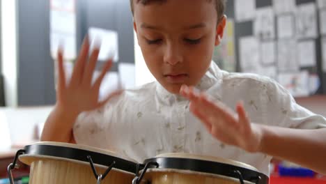 Front-view-of-attentive-Asian-schoolboy-playing-bongo-in-a-classroom-at-school-4k