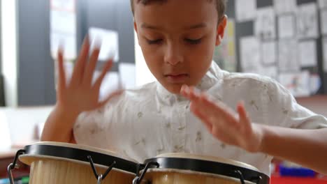 front view of attentive asian schoolboy playing bongo in a classroom at school 4k