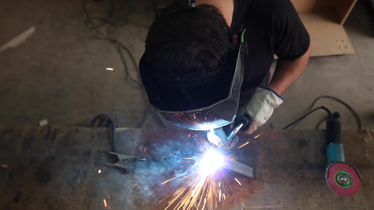 Welder in protective helmet welding metal detail in workshop