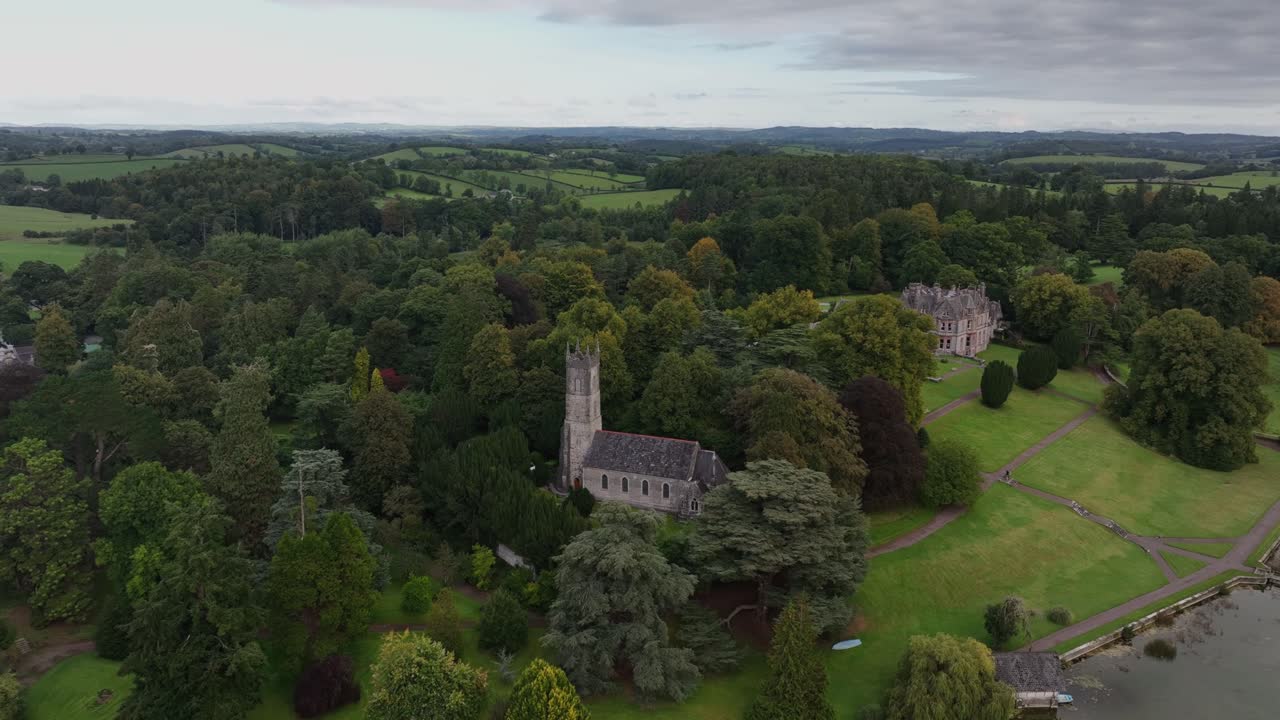 St. Salvator's Church, Glaslough, County Monaghan, Ireland, September 2022. Drone pullback and ascend framing historic building in dense thick trees overlooking grounds.