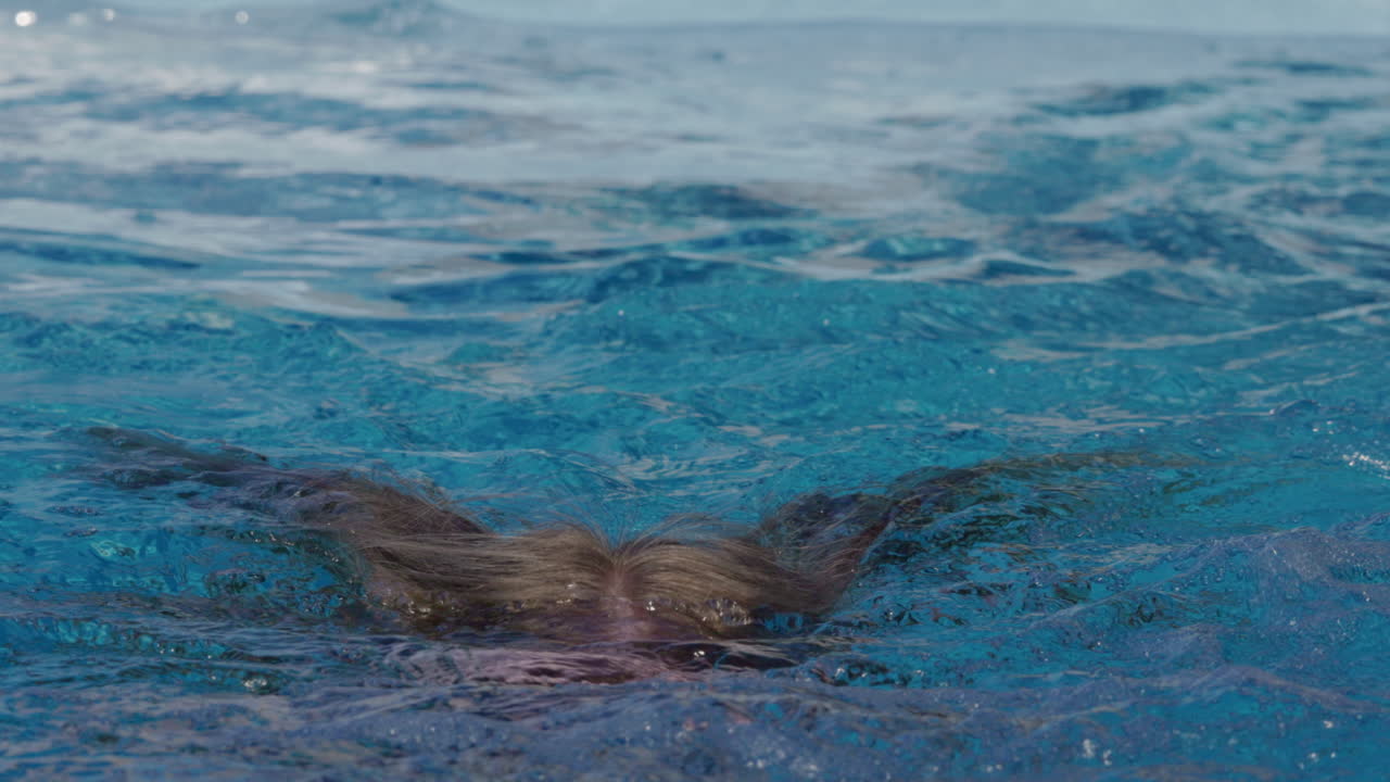 Young Woman in Sunglasses Submerging and Resurfacing in a Swimming Pool