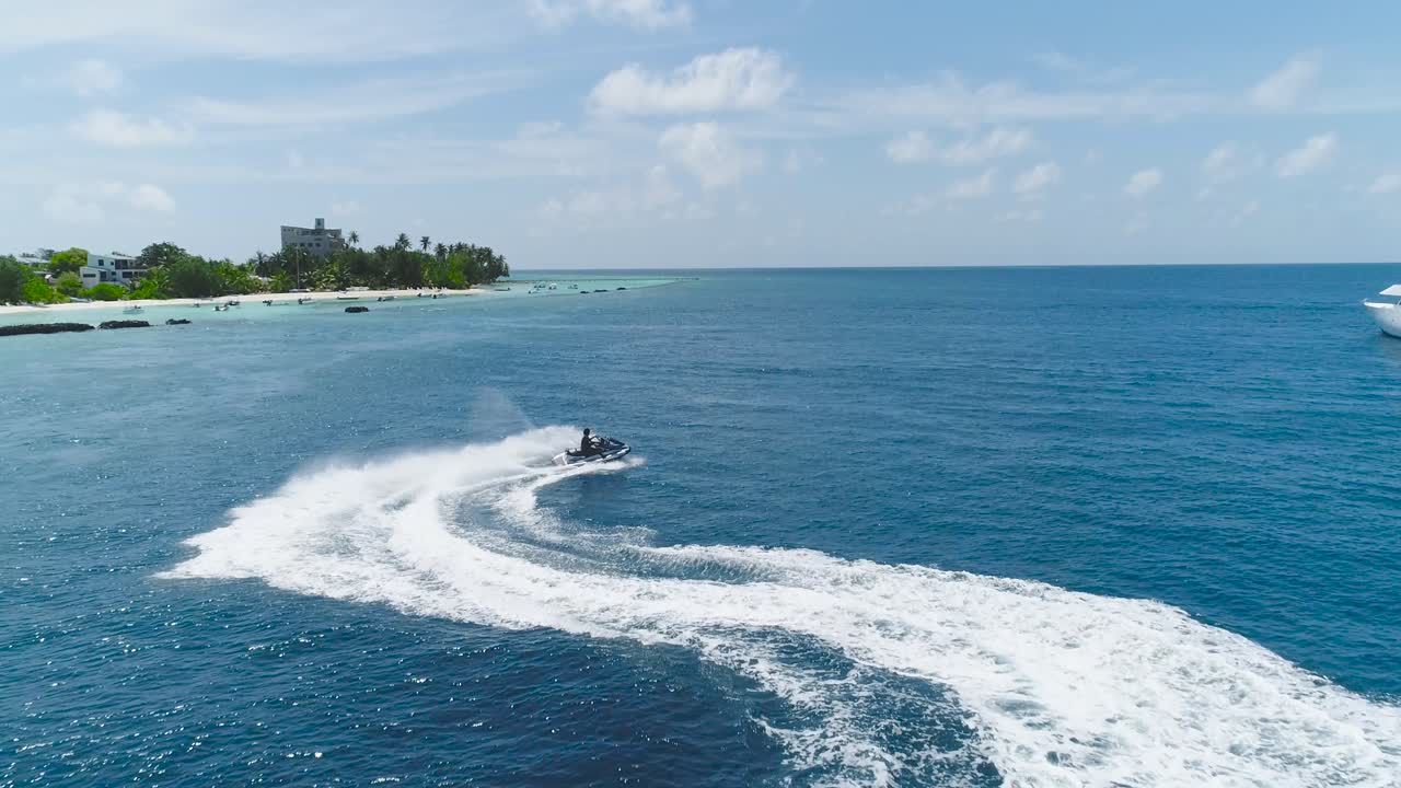 Drone tracking shot Over Man Riding A Jet Ski At Tropical Paradise Exotic Island with blue and turquoise ocean sea view. Adventure Concept for Tourist Attraction at Beach Vacation sport at Summer day
