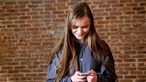 joven hermosa está viendo su teléfono inteligente, concepto de comunicación, concepto de relajación, fondo de ladrillo
