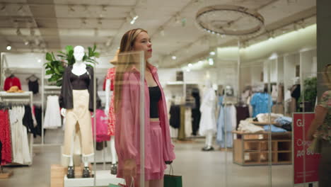 beautiful lady wearing black crop top under pink outfit walks through a fashion mall holding shopping bags, as a woman in vintage floral clothing passes by behind her, with mannequins in the mall