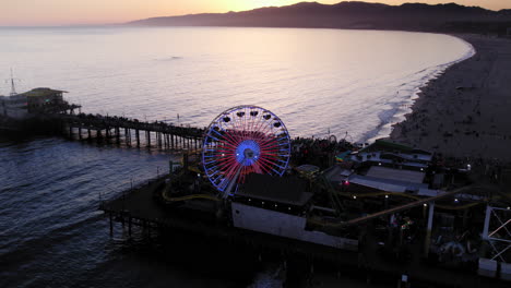 Drohnenaufnahme-Bei-Sonnenuntergang-Bei-Sonnenuntergang,-Die-Sich-Vom-Beleuchteten-Santa-Monica-Pier-Zurückzieht