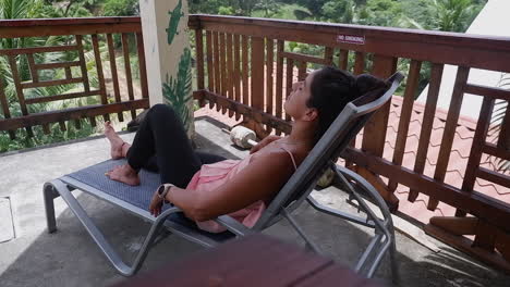 Latina-woman-lounges-in-deck-chair-on-warm-balcony-overlooking-jungle