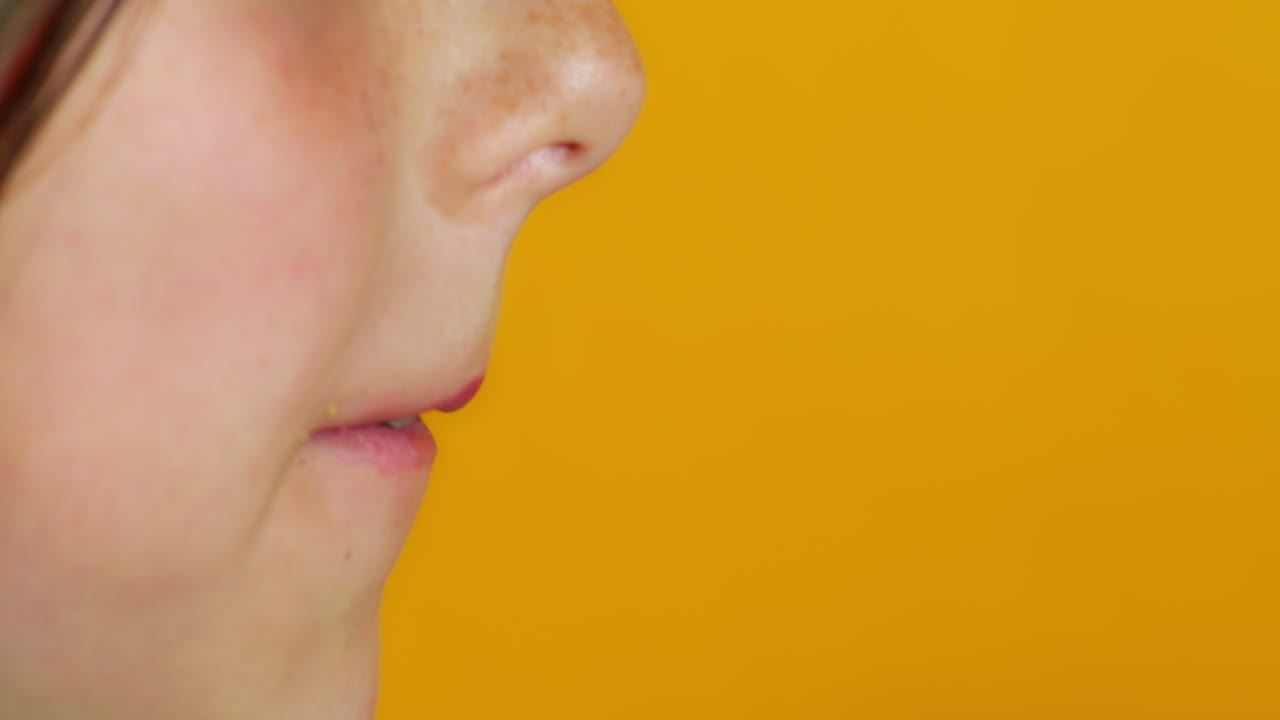 A close-up captures a child taking a big bite from a Berliner-style donut with yellow frosting and chocolate flakes, held in a hand with orange nail polish against a vibrant yellow background.