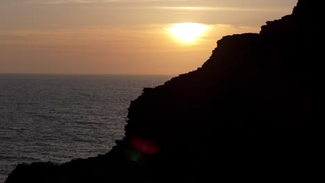 Drone-trucking-reveal-shot-from-sea-cliff-silhouette-of-golden-sunset-over-ocean