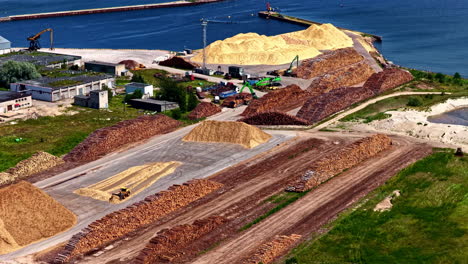 aerial view of wood processing port area with large piles of timber and sawdust near sea