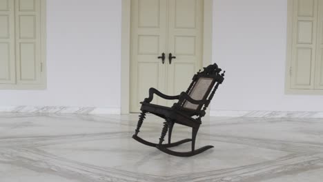 a single wooden chair rocking in front of the colonial house