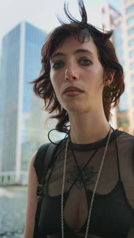 retrato vertical de moda al aire libre de una mujer joven de estilo alternativo con tatuajes y perforaciones en canary wharf en los muelles de londres filmado en tiempo real 1