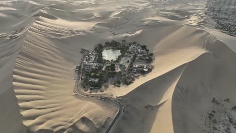 toma en órbita de un pueblo aislado rodeado de dunas de arena, ica, huacachina