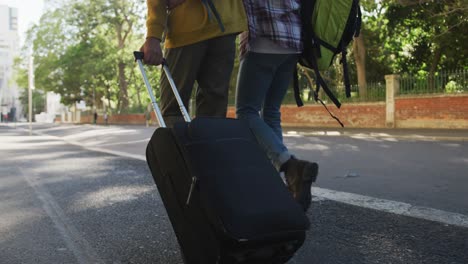 low section of two mixed race male friends walking with suitcase down the street