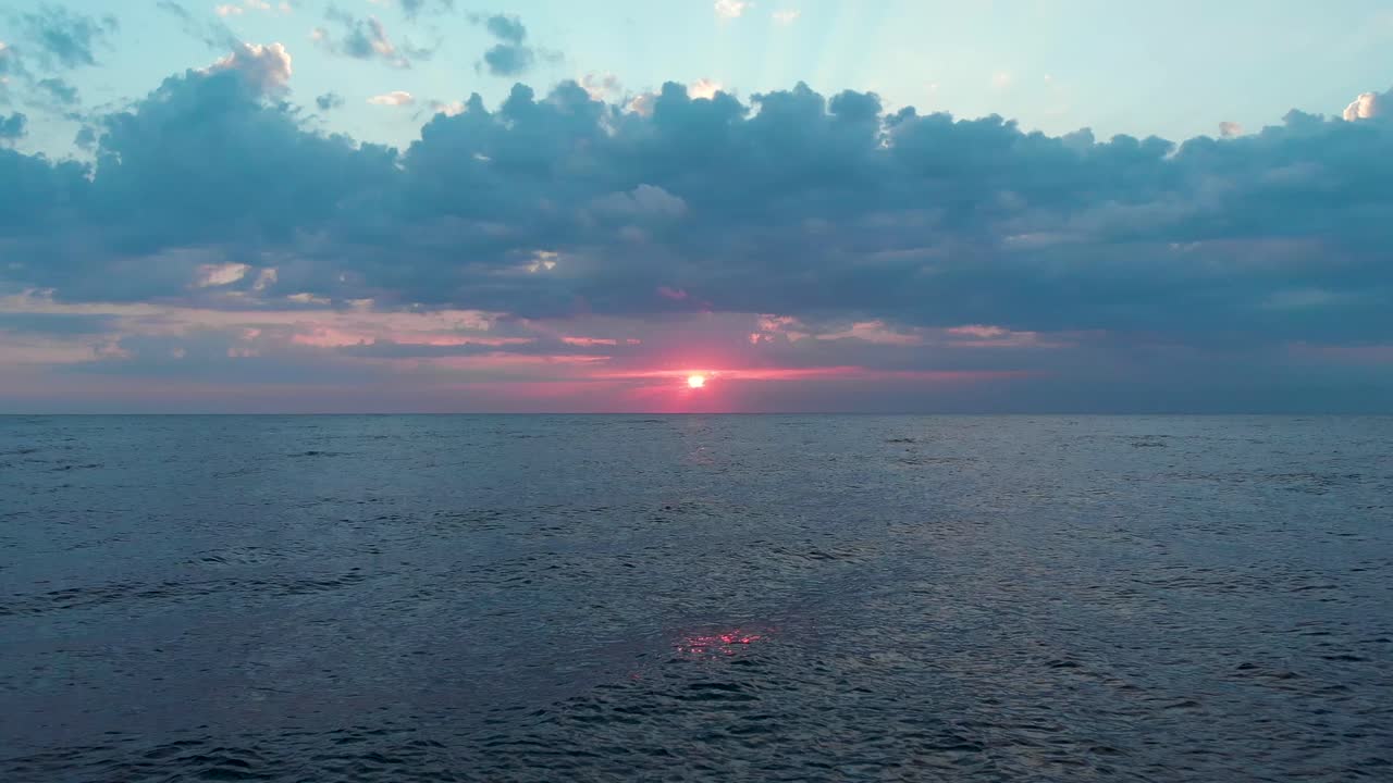 Aerial shot of the red sun rising among clouds and creating light streaks on the sky at sunrise