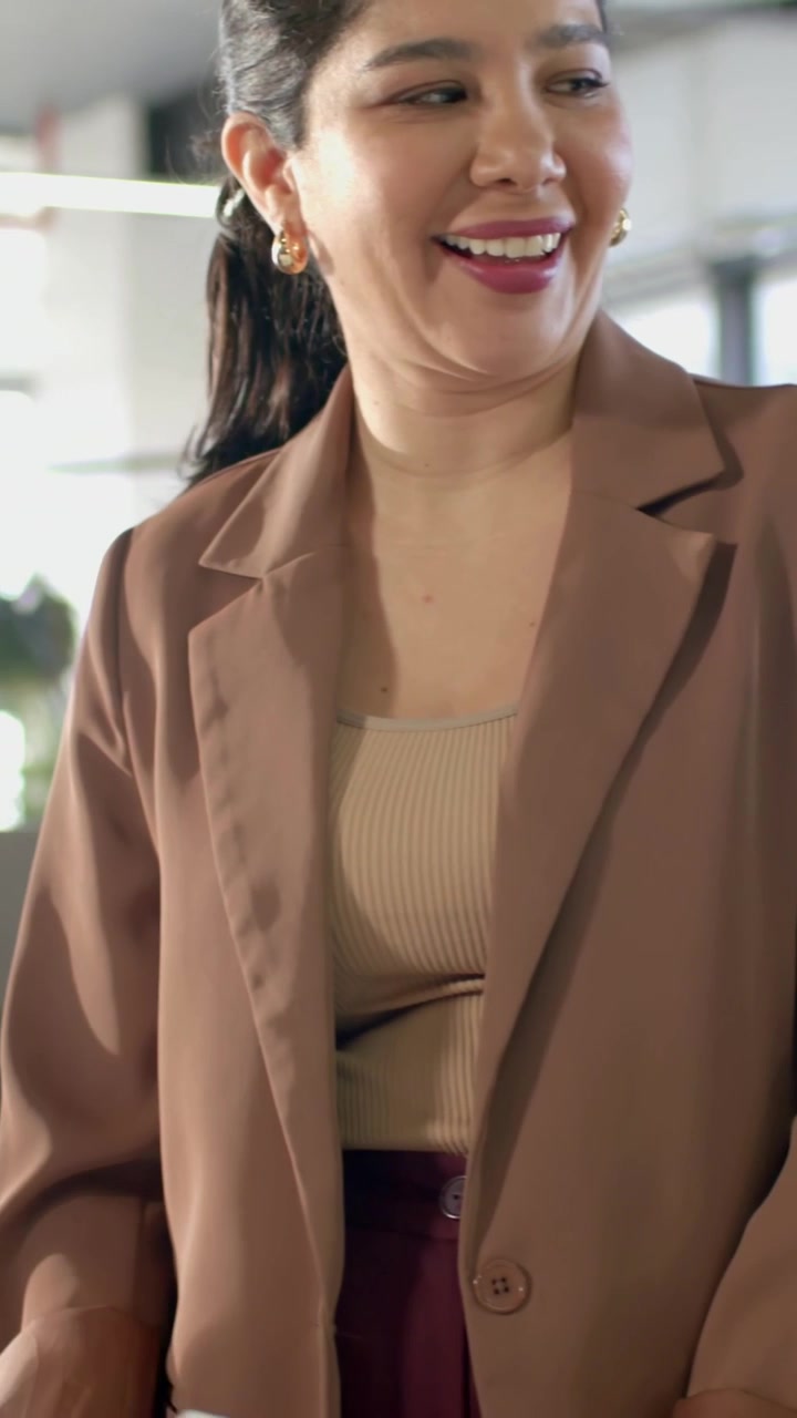 Video verticale: Donna in blazer color cammello che ascolta, si gira e risponde dopo che un collega le ha mostrato un documento.