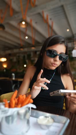 teenager enjoying sweet potato fries and using a smartphone in a cafe.