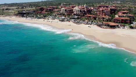 aerial, tracking, drone shot, tilting towards waves, hitting the sheraton beach, on a sunny day, in cabo san lucas, baja california sur, in mexico