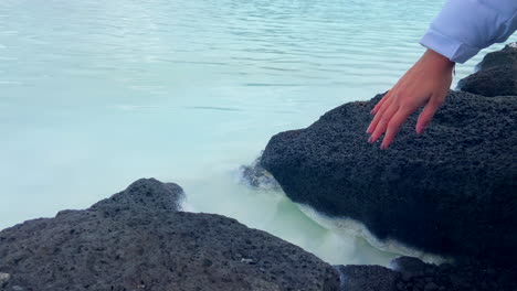 Mujer-Tocando-El-Agua-Termal-Turquesa-Entre-Rocas-Volcánicas.