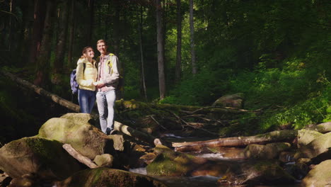 a young couple of tourists admire the forest landscape stand on a large rock near a mountain river o