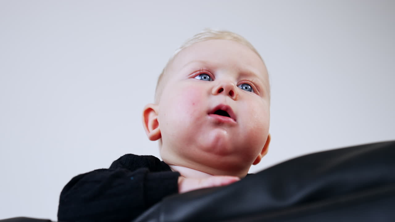 Beautiful Caucasian blond baby face standing on the sofa. Low angle view on the grey-eyed child close up. White backdrop.
