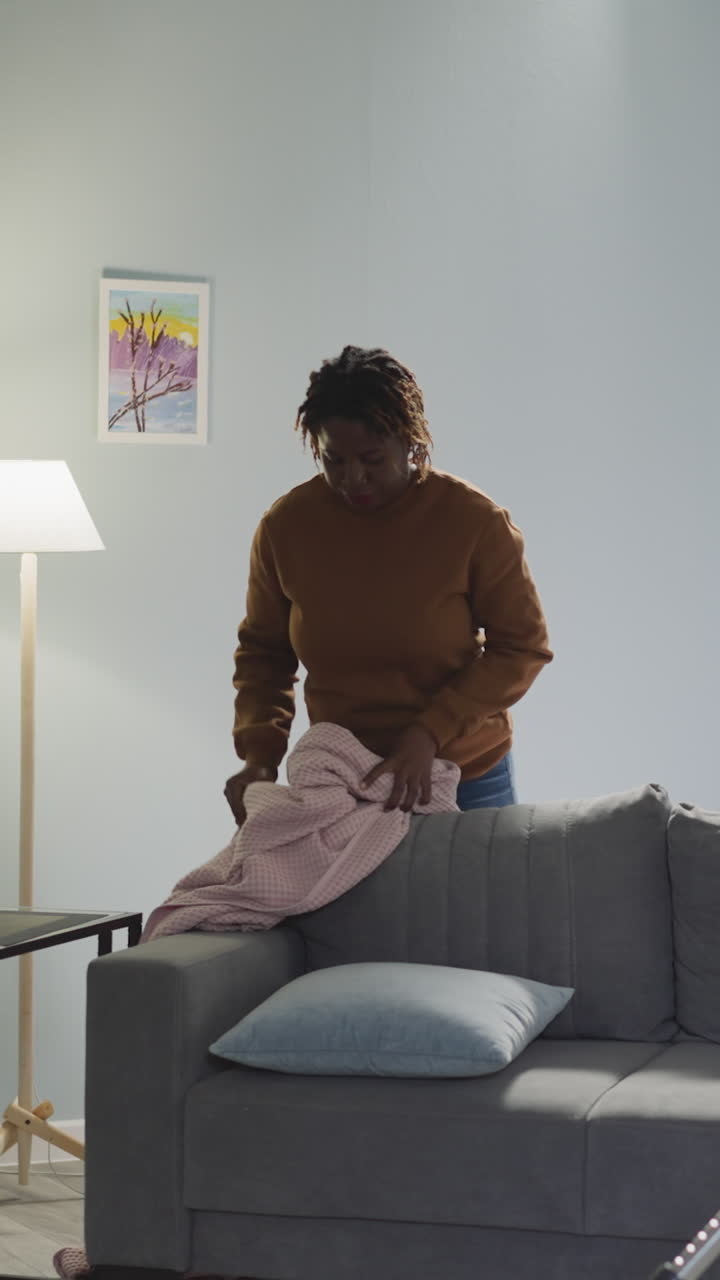 amigos multirraciales limpian la sala de estar juntos el fin de semana. mujer india aspira el piso en el apartamento mientras el compañero de cuarto afroamericano pone el cojín en el sofá