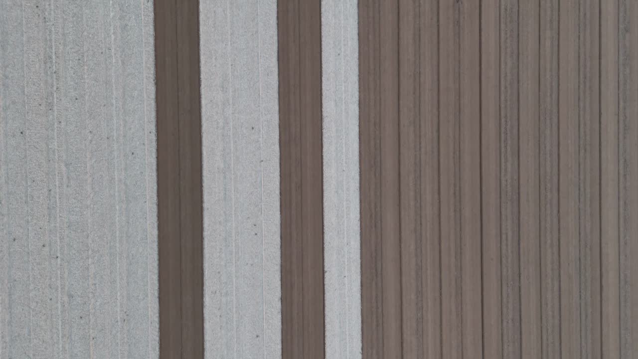 slow orbit around a tractor pulling a harrow as it carves dark seed lines through bleached soil, revealing an endless grid of fresh furrows across a vast agricultural plain under soft daylight