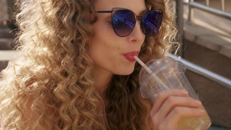 mujer con cabello rizado y gafas de sol bebiendo