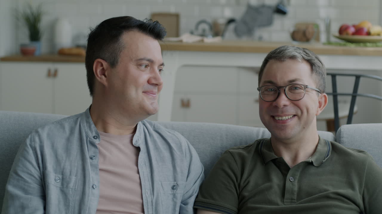 Dois homens sentados em um sofá, sorrindo e conversando