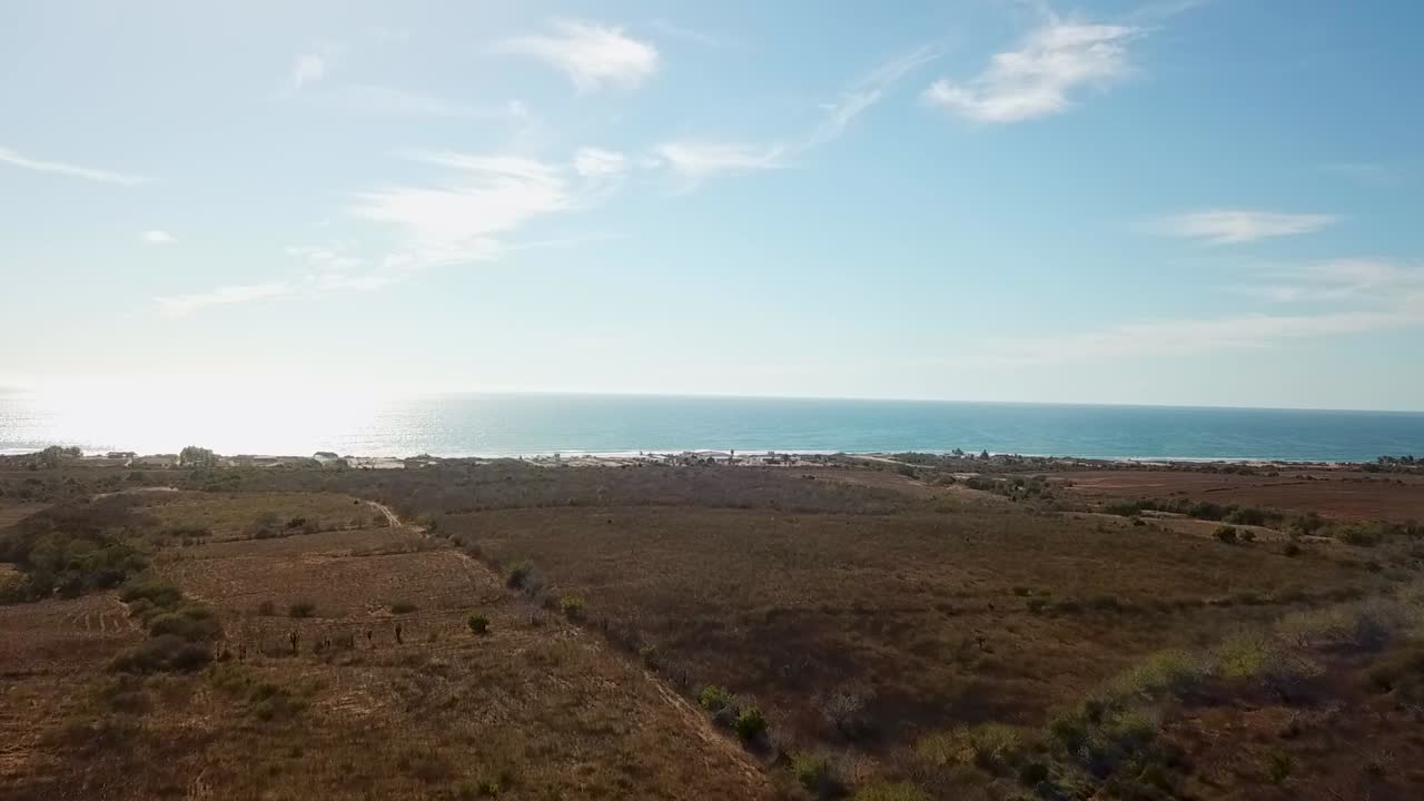 Vista aérea de drone da Costa de Sinaloa, ensolarada, à tarde, com oceano, campos, praia, estrada