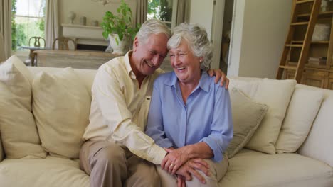 Lächelndes-Kaukasisches-älteres-Paar,-Das-Sich-Umarmt,-Während-Es-Zu-Hause-Auf-Der-Couch-Sitzt