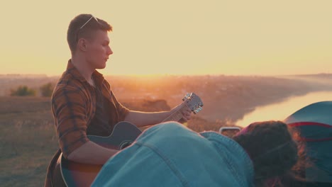 man in glasses plays guitar to happy friends near bonfire