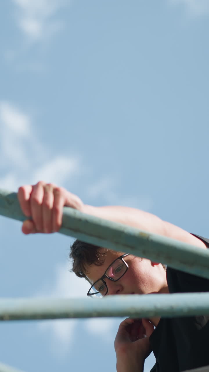 야외 푸른 철 장비에 앉아있는 어린 소년의 위쪽 시선, 그의 왼손은 철을 들고 목을 고, 공은 철 프레임 안에 혀 있습니다.