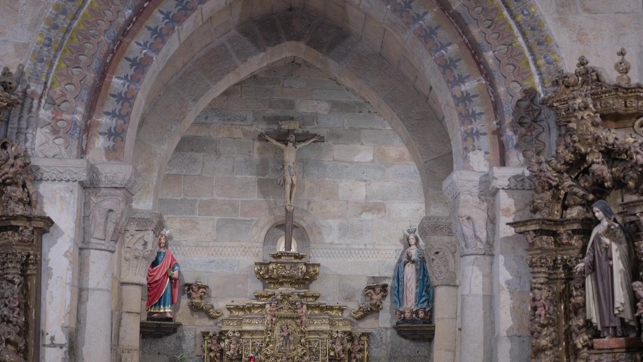 Arco in pietra dipinto che incornicia un crocifisso, un altare dorato e statue in una vecchia chiesa.