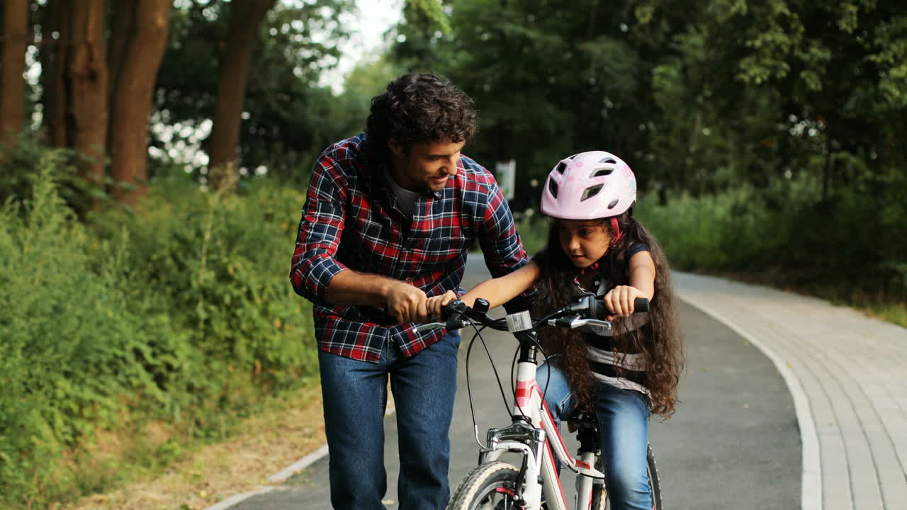 retrato de una niña y su padre. padre enseñando a su hija a montar en bicicleta. sonriendo. cámara en movimiento. fondo borroso