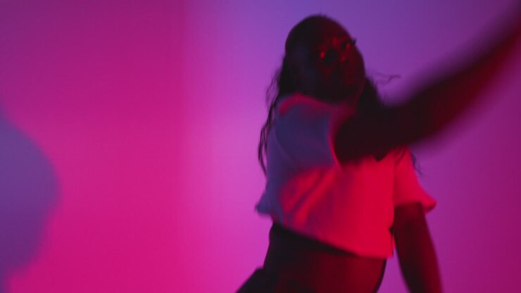 Studio Shot Of Young Woman Dancer Dancing Against Blue And Pink Lit Background