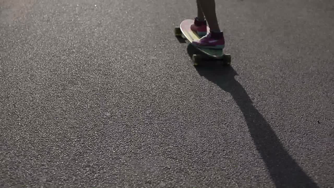 Asphalt shadow of a girl riding with skateboard in the hand on the way.