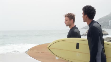 Seitenansicht-Von-Zwei-Männlichen-Surfern,-Die-Mit-Surfbrett-Am-Strand-Stehen-4k