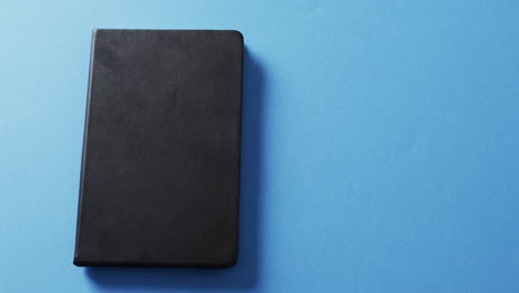 primer plano de un libro negro cerrado con espacio de copia en un fondo azul en cámara lenta