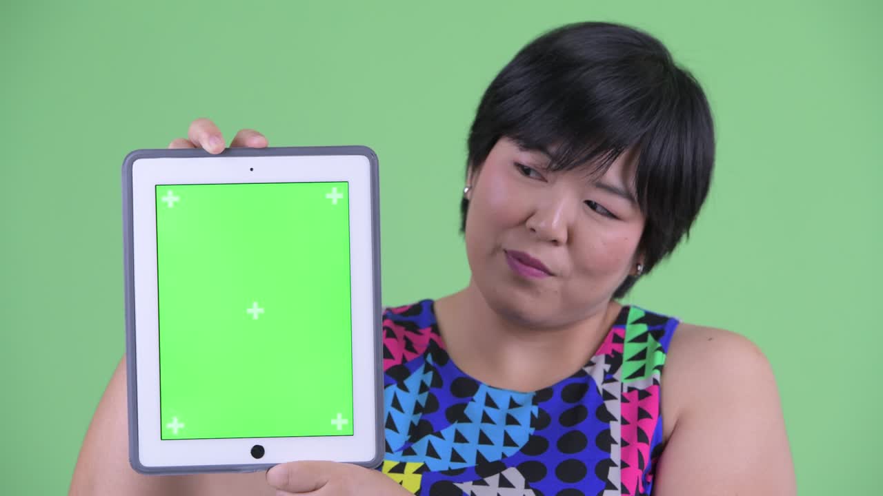 아시아 여성이 녹색 배경에 크로마 키 복사 공간을 가진 디지털 태블릿을 보여줍니다.