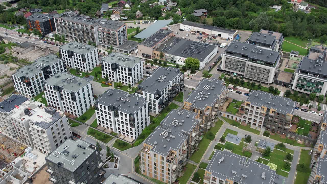 Drönare glider över mellanhöga bostadsrättskomplex, innergårdar och blandade byggnader i Markučiai, Vilnius, och visar gatunät, hustak och grön landskapsarkitektur