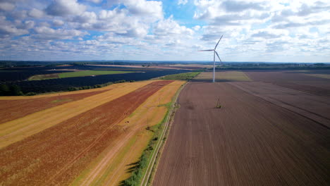 Luftwagen-Gleiten-über-Farbenfrohes-Landwirtschaftliches-Ackerland-Mit-Windturbinen,-Die-Sich-Langsam-Im-Wind-Drehen