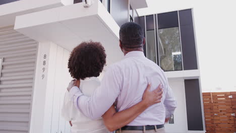 middle aged black couple stand outside admiring their modern home, close up,  back view