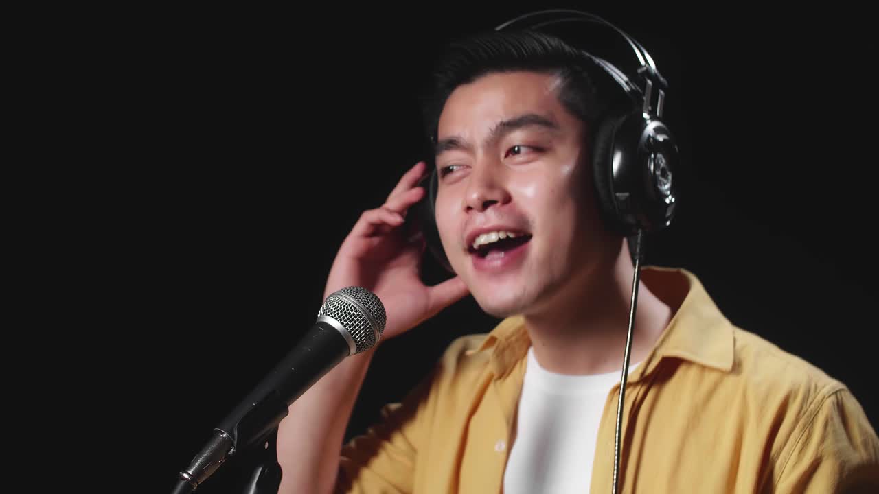 Side View Of Asian Man Singer Wearing Headphone And Singing Into Microphone On Black Background