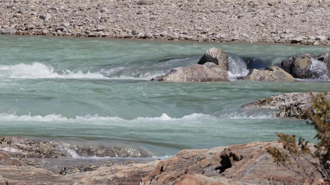 Rio glacial de montanha turquesa flui sobre afloramentos rochosos do leito do rio.