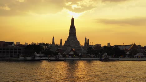 bangkok,wat arun temple during breathtaking sunset from a distance,boats crossing in front of the majestic chao phraya river.zooming out.