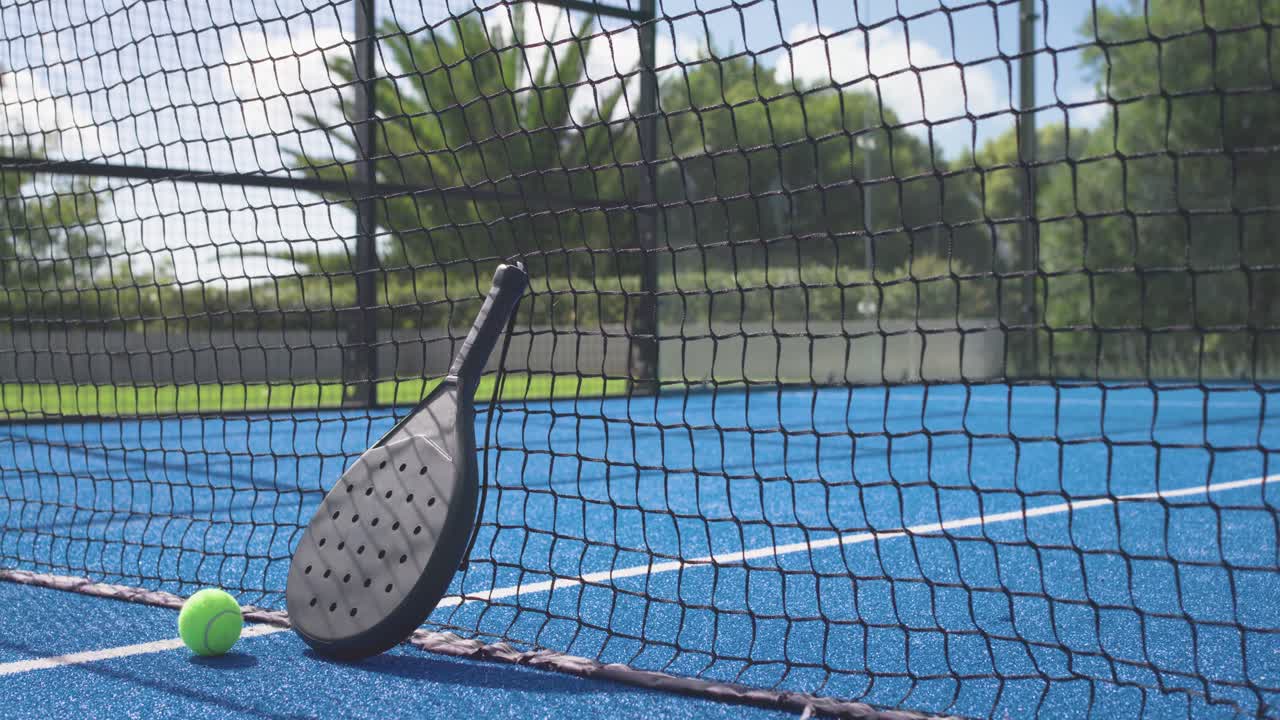 Tilting-pulling camera is revealing paddle leaning against net and green ball on court to showcase
