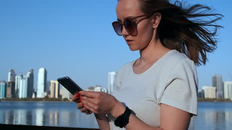una chica con el pelo largo marca un mensaje en el teléfono inteligente en el muelle de dubai
